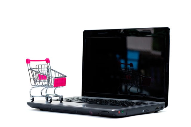 Shopping cart or supermarket trolley with laptop notebook isolated on white background, e-commerce and online shopping concept.